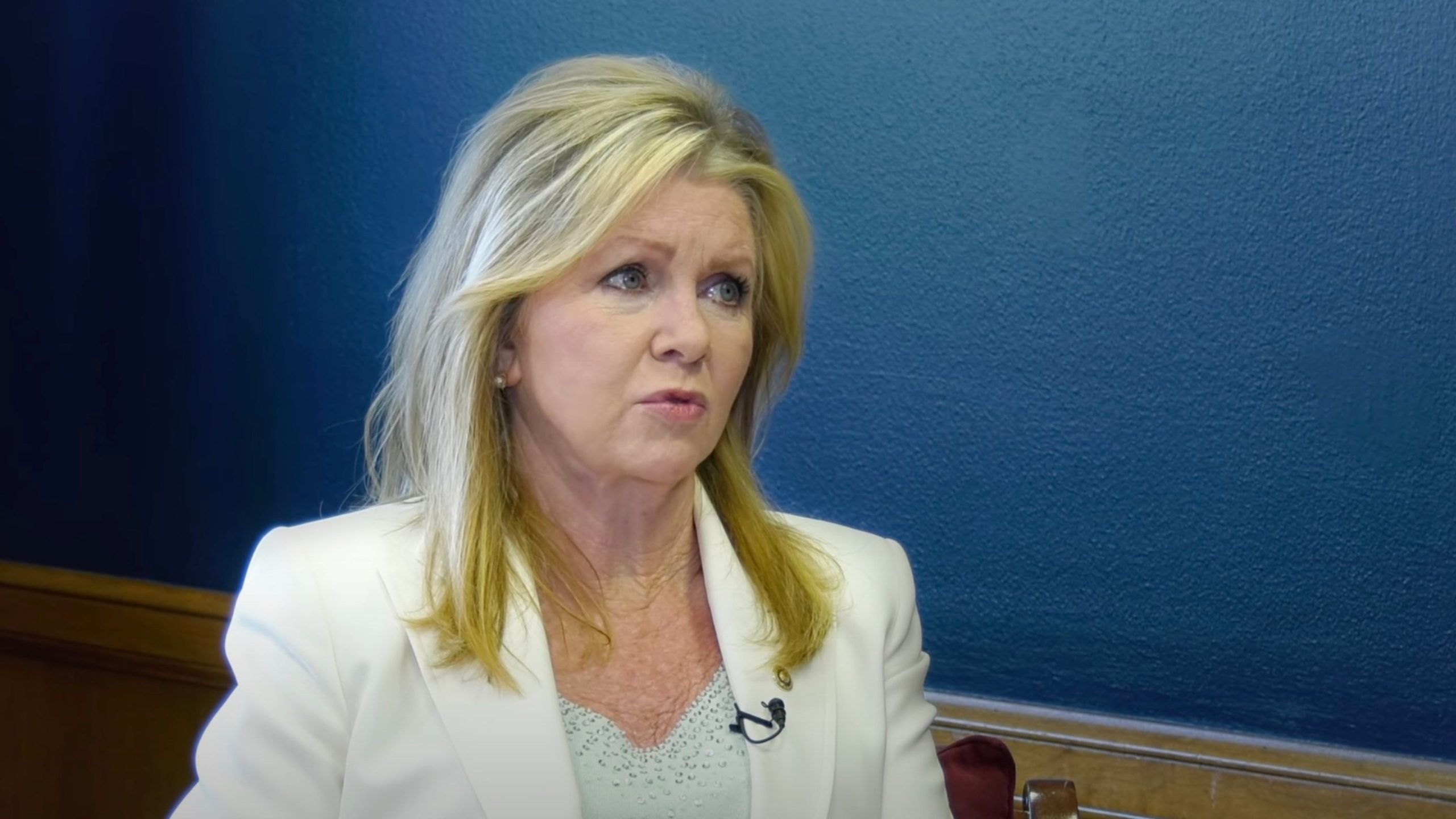 Blackburn with blonde hair wearing a white blazer sits in front of a blue background.