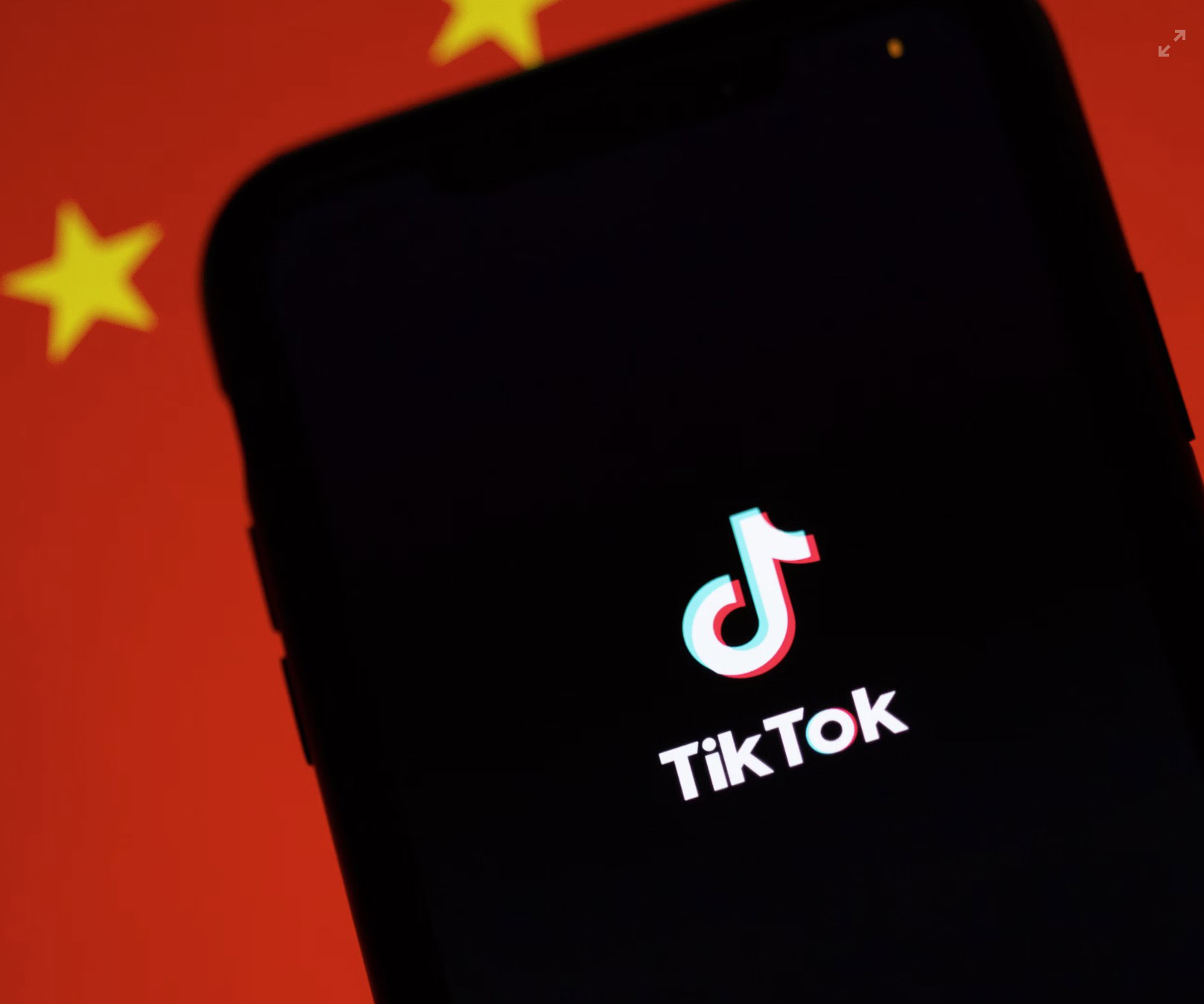 A smartphone screen displaying the TikTok logo with a blurred Chinese flag in the background.