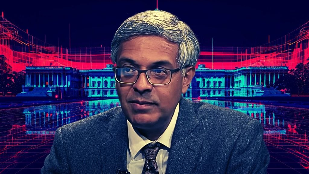 Bhattachary wearing glasses wearing a suit and tie is in the foreground, with a digitally altered image of a classical building in blue and red in the background.