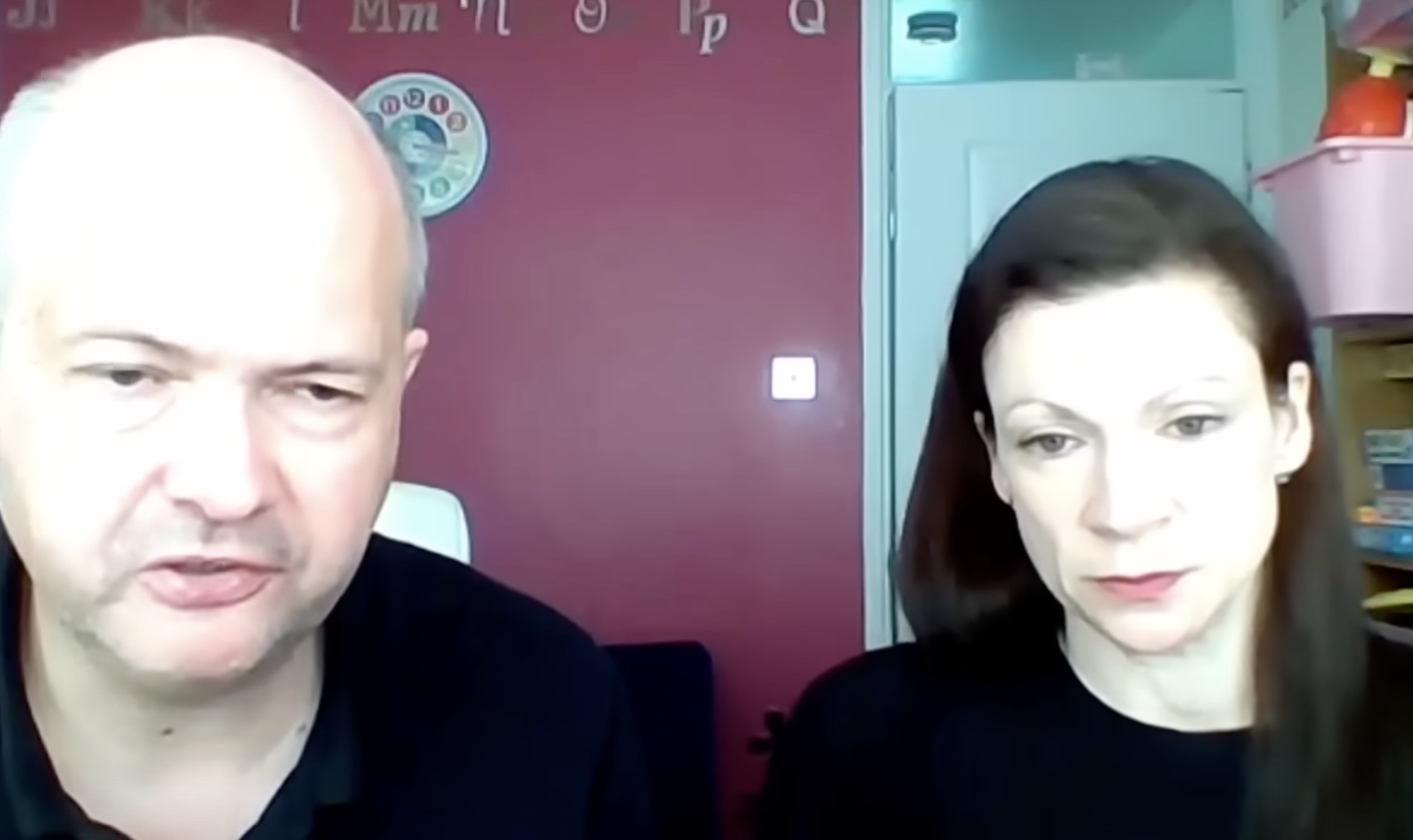 Allen and Levine sitting indoors against a maroon wall with alphabet letters on it.