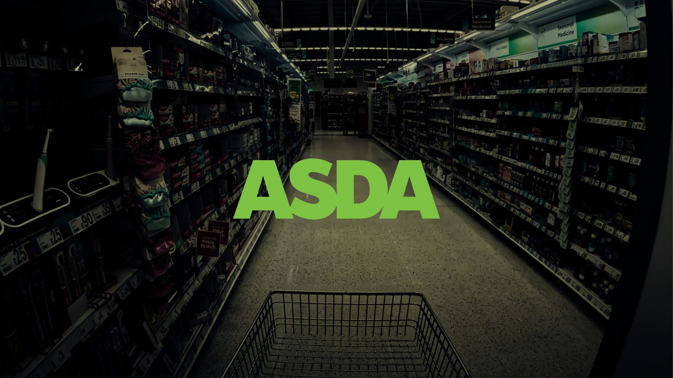 View down an empty supermarket aisle with shelves stocked on both sides and a shopping cart in the foreground, overlaid with the green ASDA logo in the center
