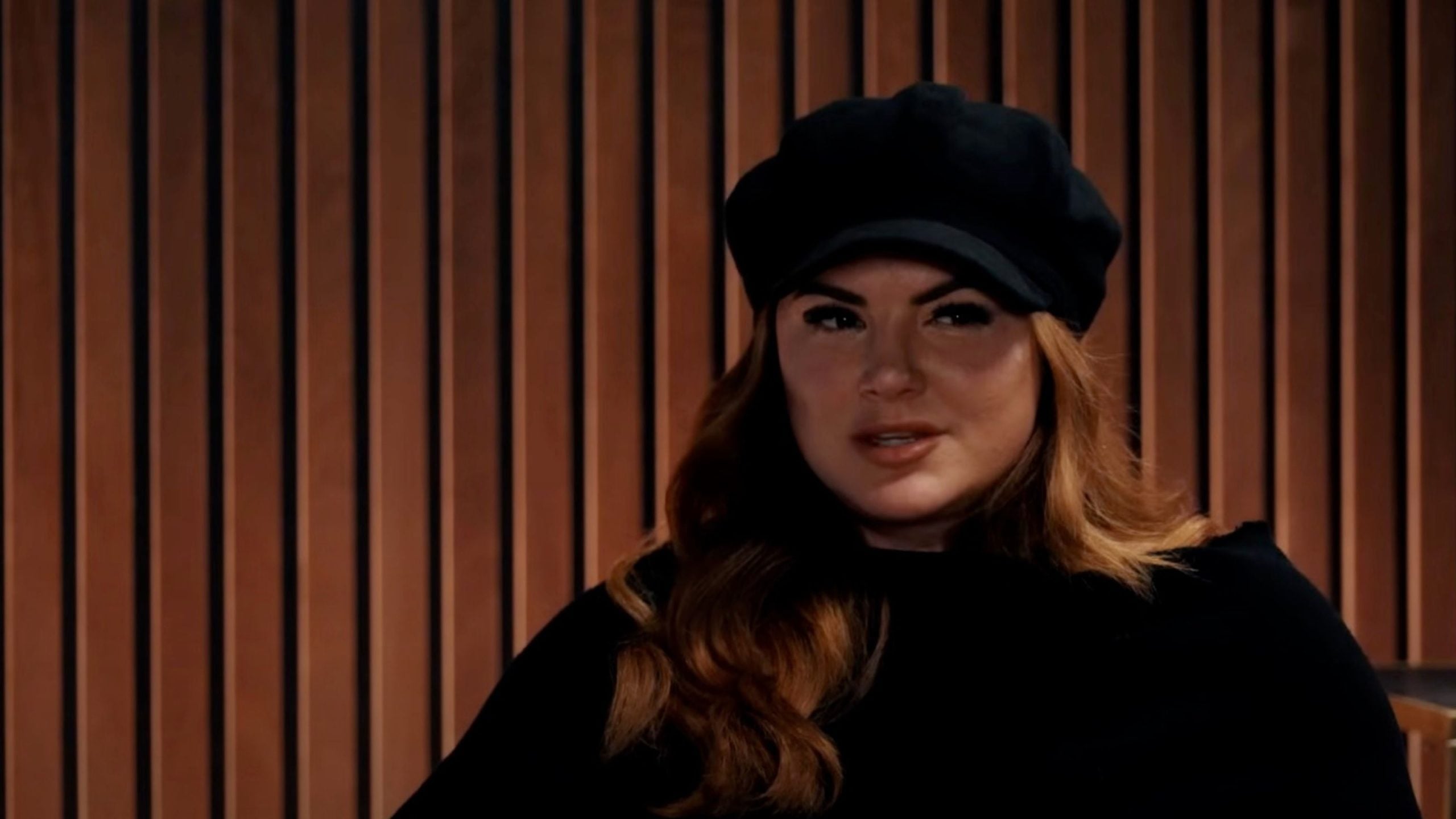 Carano wearing a dark cap and a black top in front of a wooden slat background.