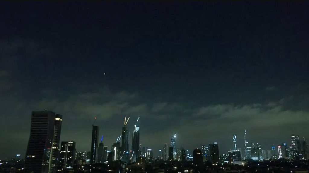 Nighttime city skyline with numerous illuminated skyscrapers under a mostly clear dark sky with some scattered clouds.