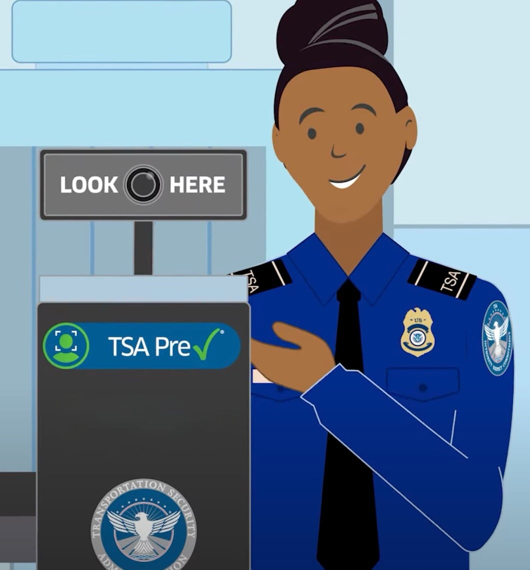 Illustration of a smiling Transportation Security Administration officer in a blue uniform pointing to a TSA Pre✓ sign with a camera and text reading "Look Here" above it at a security checkpoint.