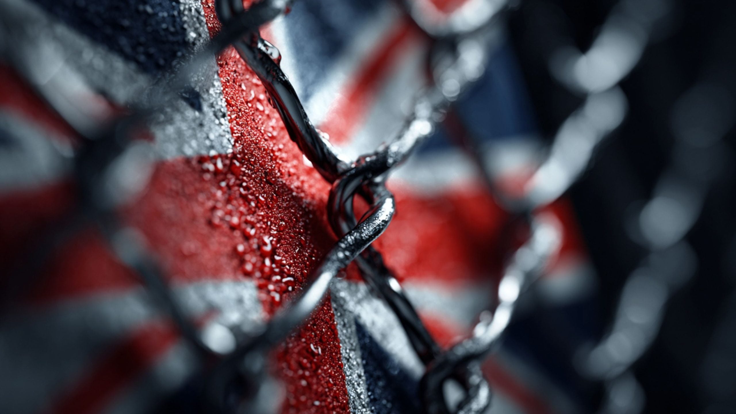 Close-up of a wet metal chain against a background resembling the Union Jack flag with water droplets on the surface.