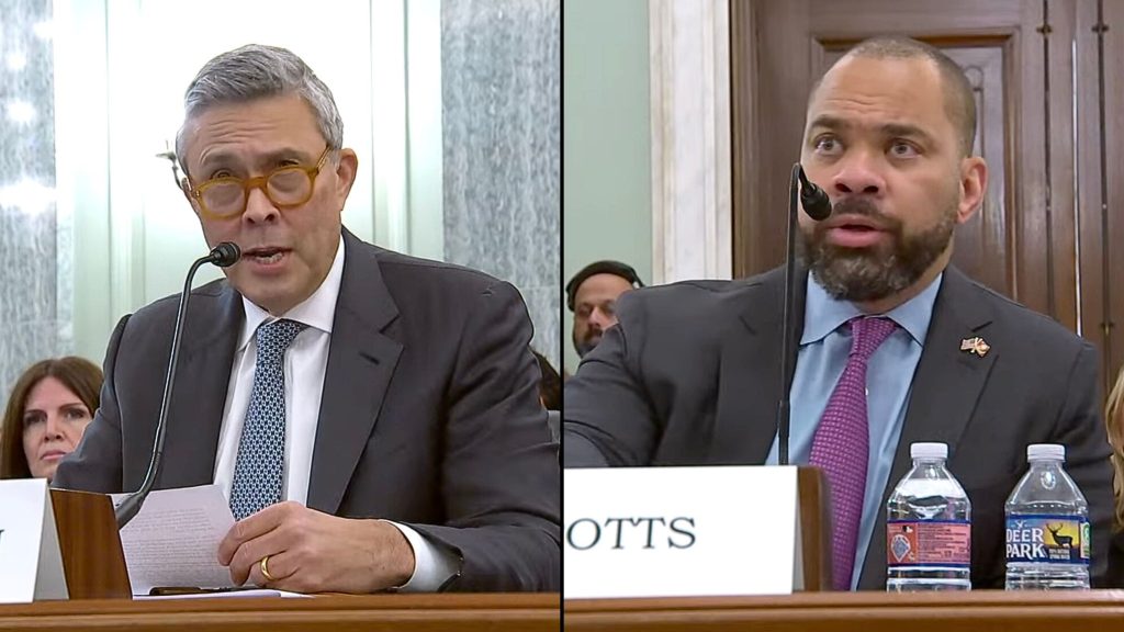 Split-screen hearing scene showing two men testifying: left, an older man with gray hair and round amber glasses in a suit holding papers and speaking into a microphone; right, a bearded man in a suit and purple tie speaking into a microphone with water bottles and a partial nameplate in front of him.