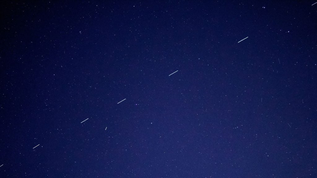 Dark night sky dotted with stars and several short, parallel white light trails crossing the frame.