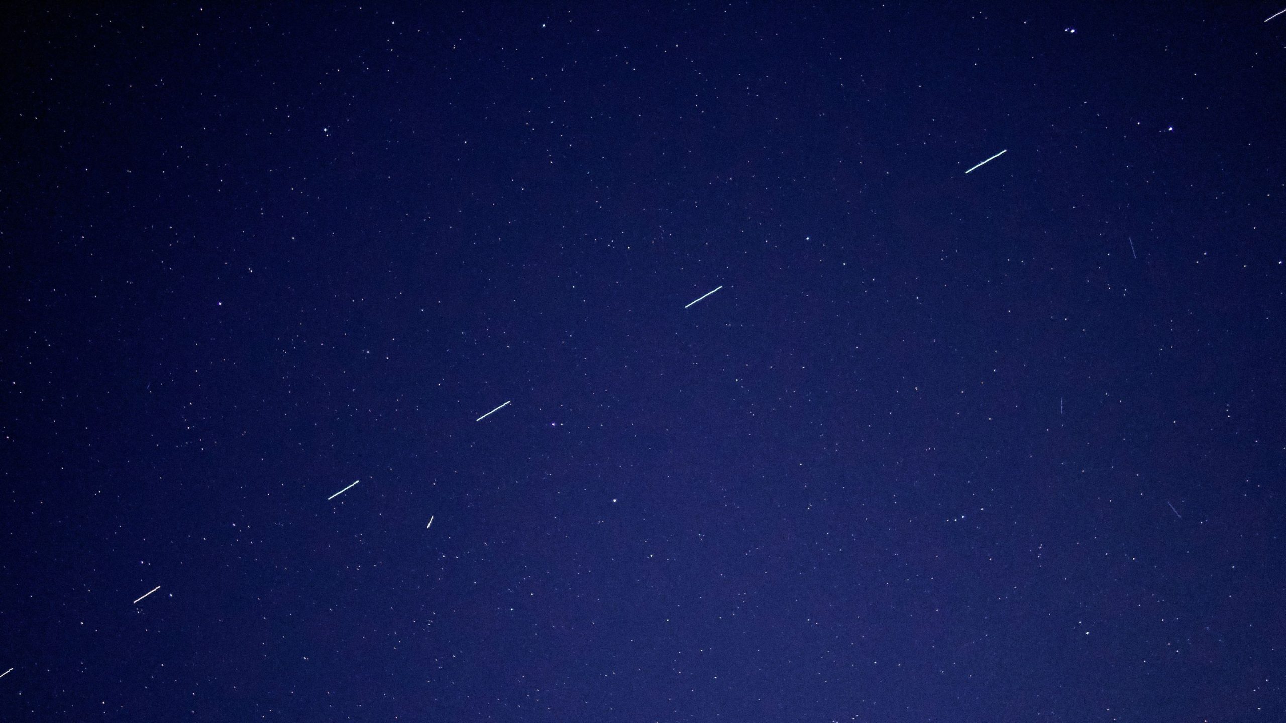 Dark night sky dotted with stars and several short, parallel white light trails crossing the frame.