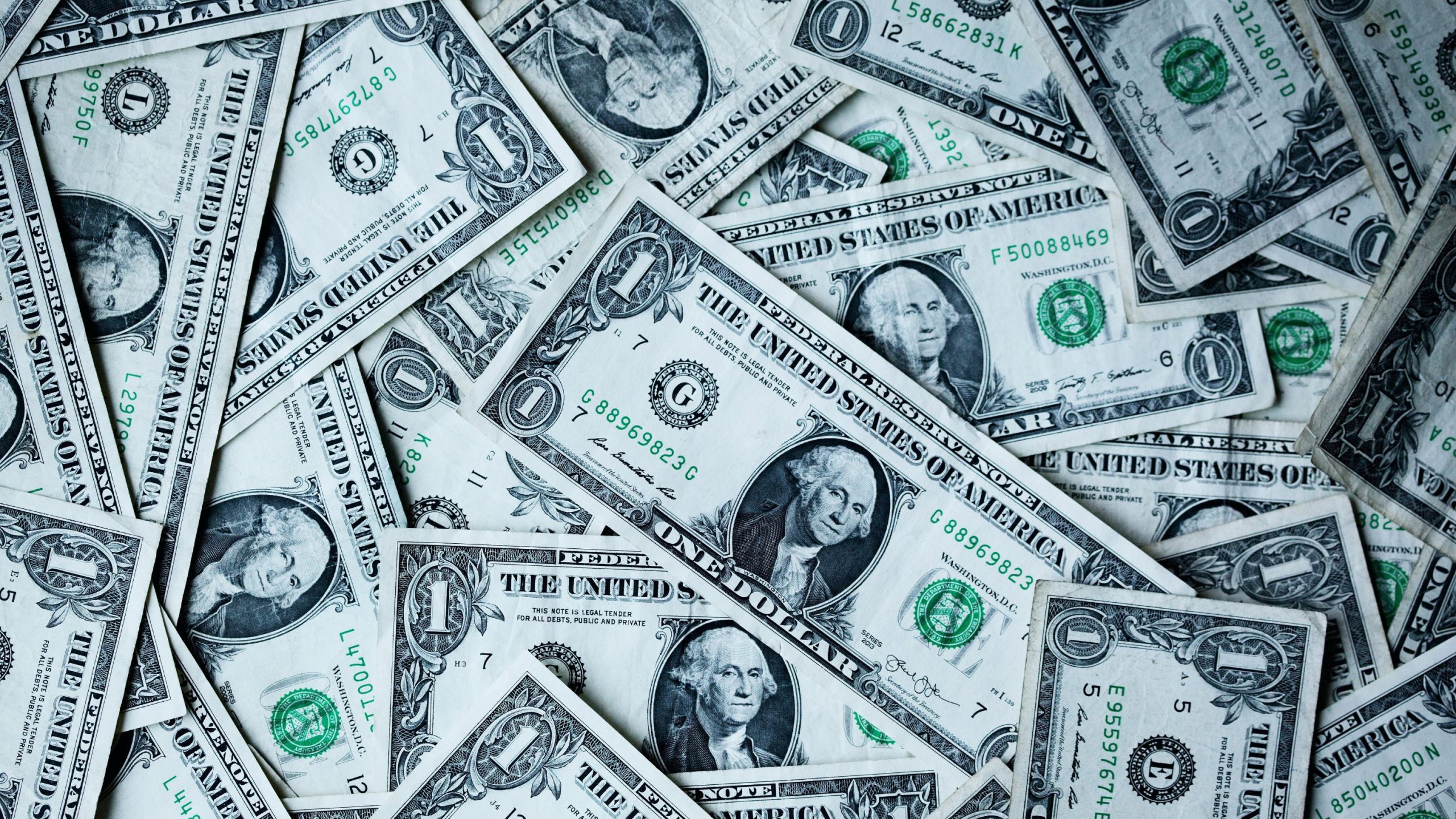 Close-up of overlapping United States one-dollar bills showing central portrait, large 1 numerals, and green Treasury seals.