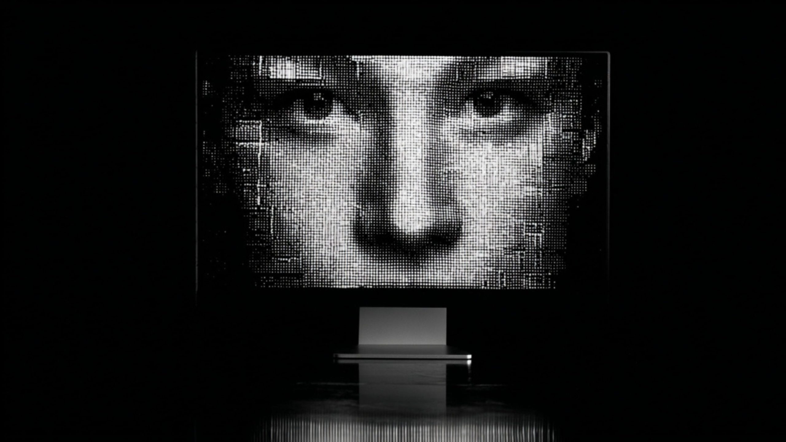 Close-up black-and-white halftone face displayed on a large screen above a minimalist pedestal in a dark room.