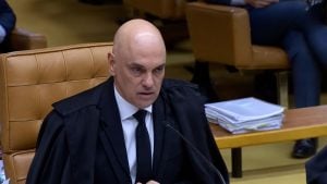 Moraes in a black robe and tie speaking into a microphone while seated at a desk with stacked documents.