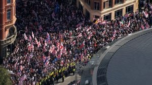 Large crowded street protest with many people waving Union Jack and St George flags between city buildings, police in high-visibility vests lining the road.