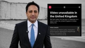 Yusuf in a dark suit and blue tie standing outdoors by a pale chalk cliff, with a black overlay reading "Video unavailable in the United Kingdom."