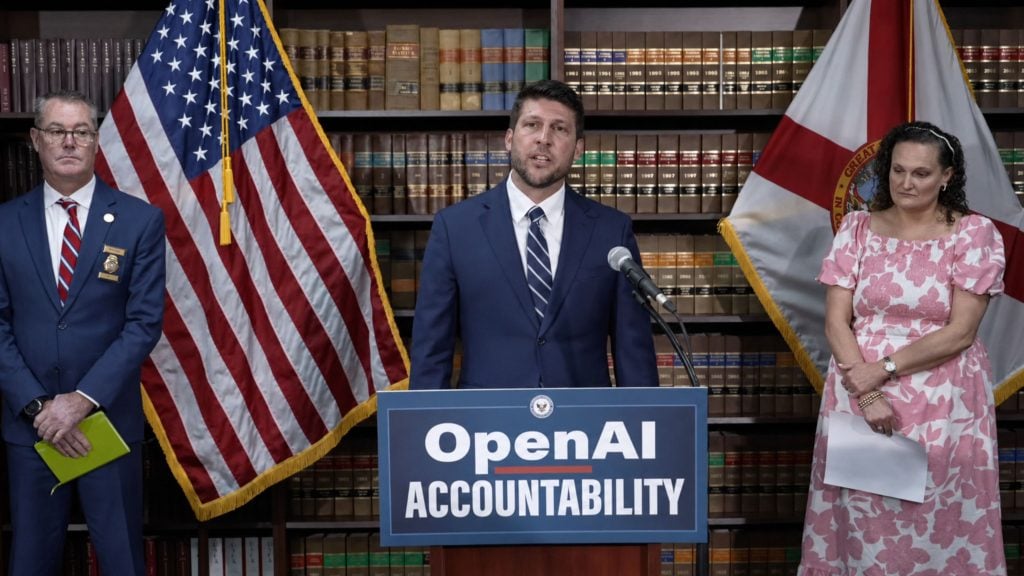 Uthmeier in suit speaking at podium labeled "OpenAI Accountability" between American and state flags, flanked by two officials in front of bookshelves.