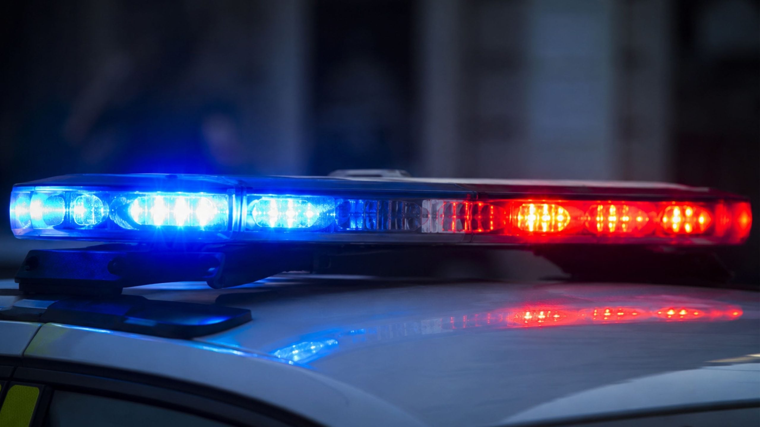 Flashing red and blue police car light bar glowing on a vehicle roof at night, reflected on the hood
