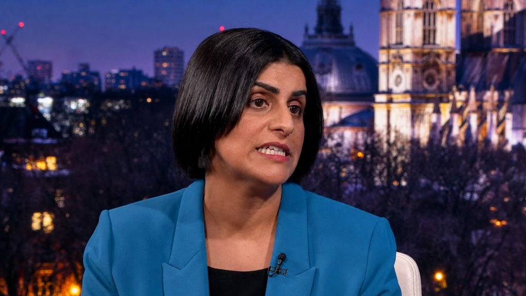 Mahmood with short black hair and teal blazer speaking on a nighttime city backdrop, wearing a lapel microphone
