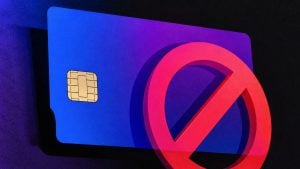 Blue credit card with visible gold chip partially obscured by a red prohibition symbol on a dark background