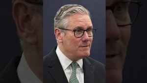 Starmer with gray swept-back hair and glasses wearing a dark suit, white shirt and patterned green tie against a dark background.